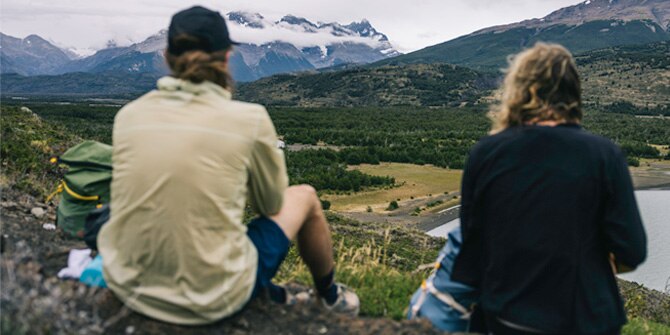 Two people sitting on a mountain looking at the view