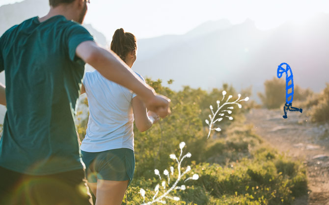 A man and woman run on a mountainous trail in sunny weather.