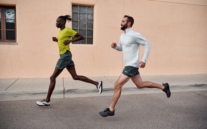 Two runners run side-by-side on a city road.