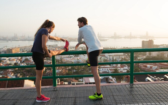 Two runners use a fence to help stretch after running.