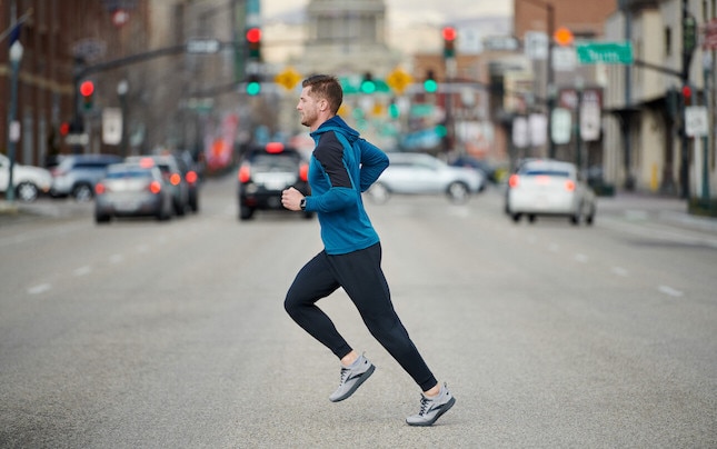 Vue latérale d’un coureur qui traverse une voie urbaine achalandée.