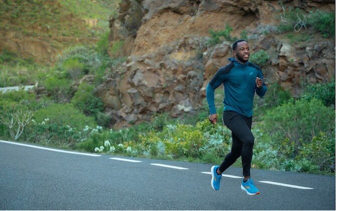 A man running down a road with a lush hill behind him