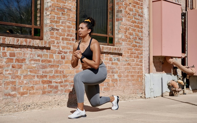 A runner does a forward lunge on a sidewalk as part of her strength training routine.