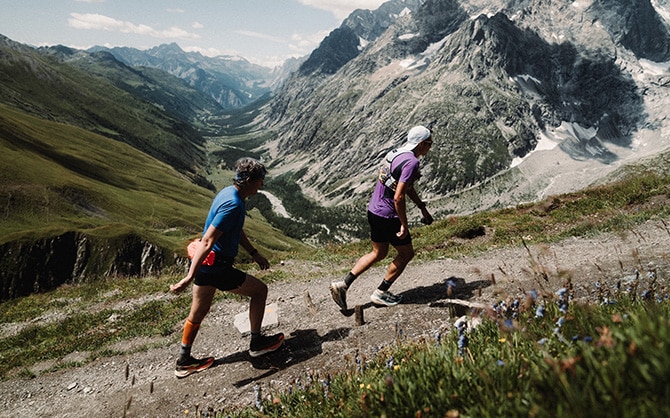 Trail runners on an alpine mountain path with scenic valley views.