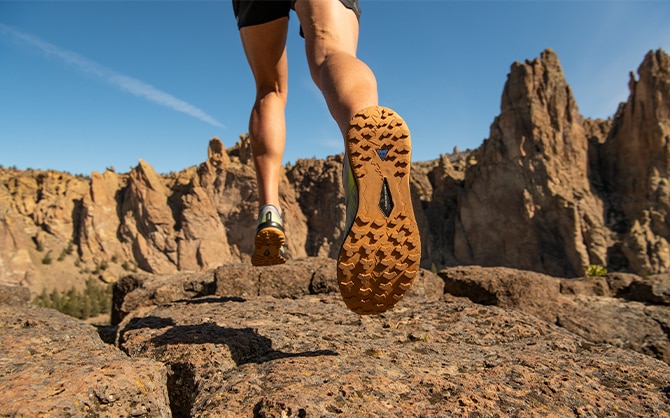 Die Unterseite eines Laufschuhs, der über Felsen läuft.