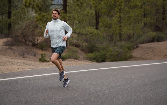 Man running on an empty road with evergreen trees in background