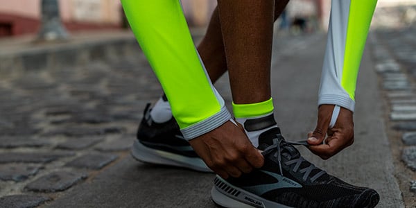 Un gros plan d’un coureur portant de l’équipement de la collection Brooks Nightlife et se tenant debout pour attacher ses chaussures. 