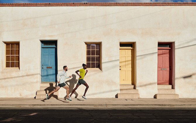 Two men running on sidewalk in front of building with colored doors