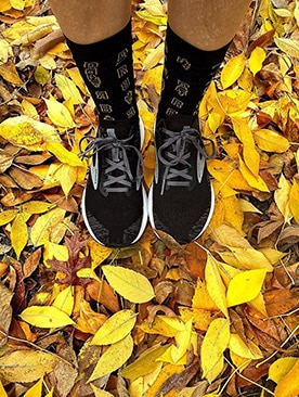 A detail photo of a runner sporting Thanksgiving themed socks while standing on gold fallen leaves. 