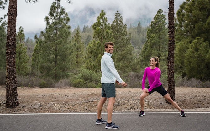 Two runners perform dynamic exercises to warm up before running.