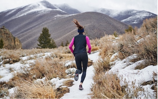 Runner on a snowy trail surrounded by hills.