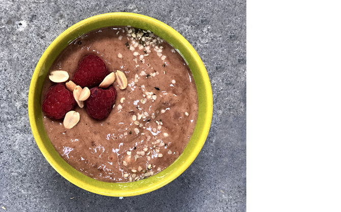 Une photo de haut en bas d’une mousse au chocolat et au chia garnie de framboises fraîches, d’arachides et de sirop d’érable.