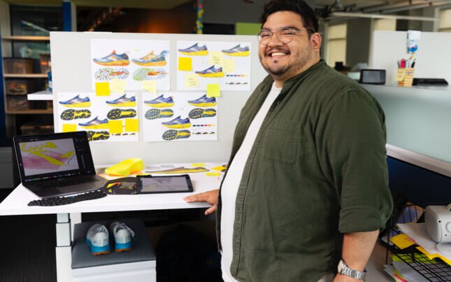 Un homme debout devant un bureau avec des dessins de chaussures