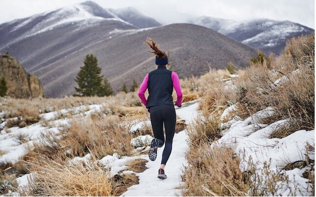Un runner sur un sentier enneigé entouré de collines.