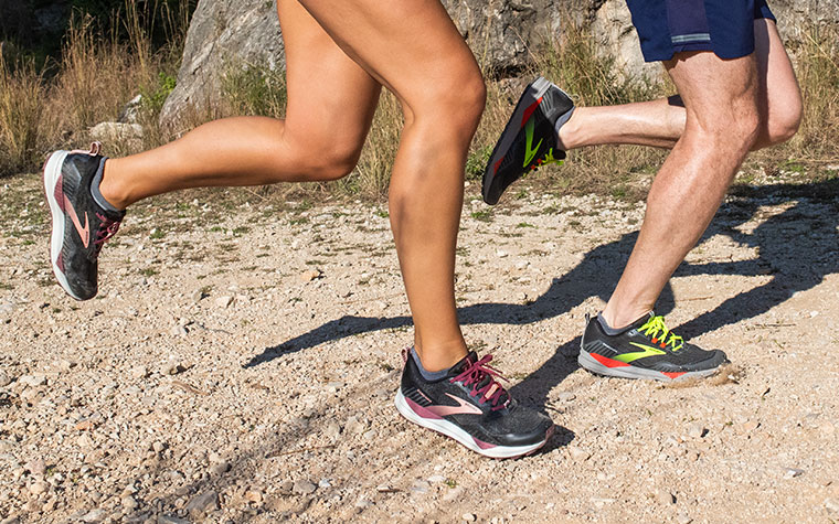 Close-up of two runners’ legs in the Cascadia, striding along a trail.