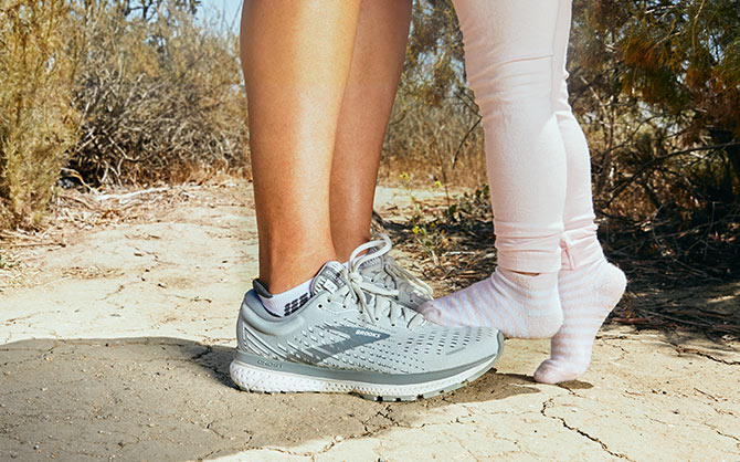 A little kid standing on a pair of Brooks shoes
