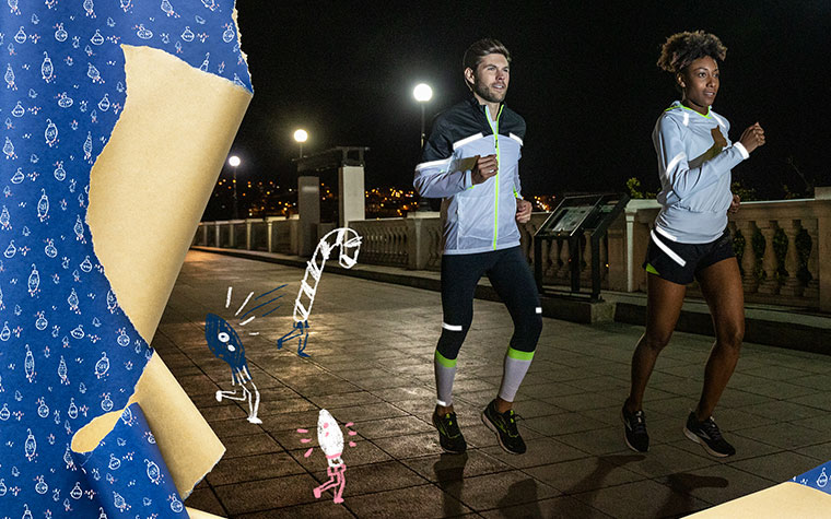 Un homme et une femme portant des vêtements réfléchissants Brooks Run Visible courent le soir.