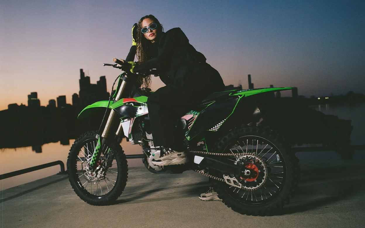 Une femme portant des chaussures Brooks assise sur une motocyclette, avec un coucher de soleil en arrière-plan