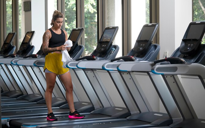 Frau steht auf dem Laufband im Fitnessstudio mit einem Handtuch in der Hand