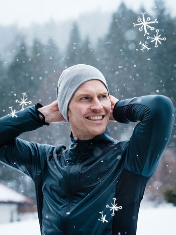 A smiling man putting on a beanie as he gets ready for a run in the snow. 