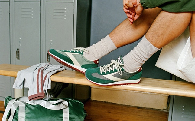 Close up of someone wearing the green Brooks Vanguard shoes in a locker room with their feet on the bench