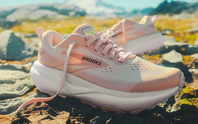 Close up of the Cascadia 20 trail running shoes in a pink colorway positioned on a rocky mountain