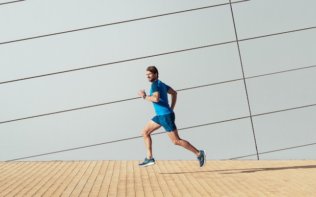 A runner looks to the side while running on a city pavement.