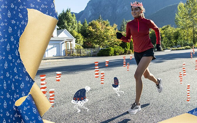 A runner wearing a read long sleeve half zip and shorts runs on a road with mountains in the background.