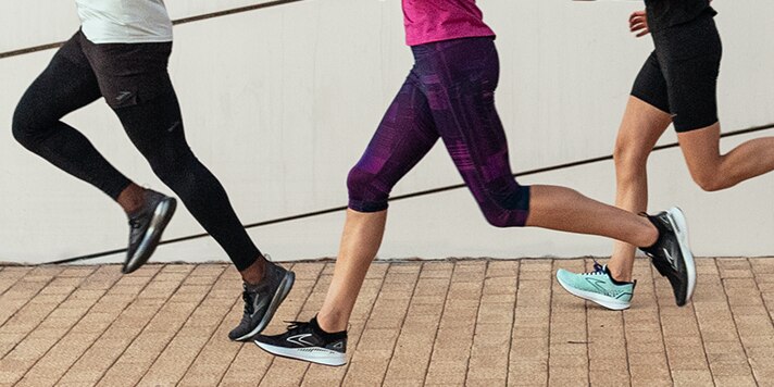 Four individuals run together as a group across a cobble-stone square.