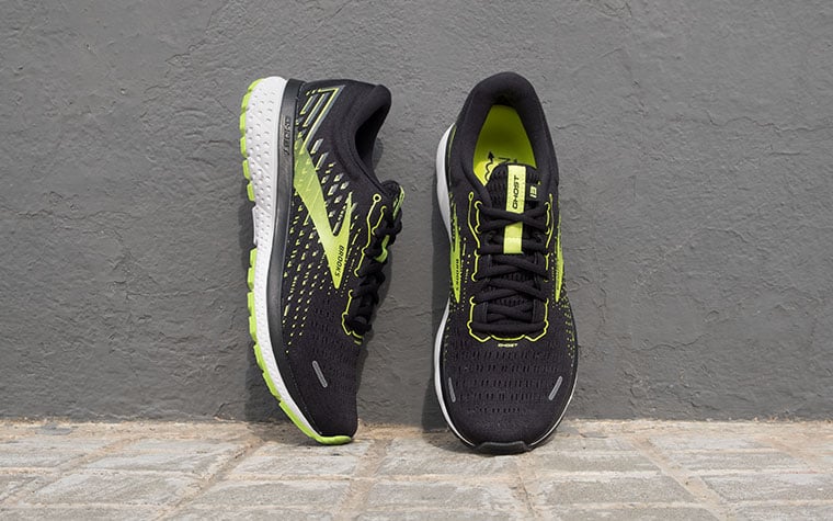 A pair of black and green Ghost shoes lean against a grey wall.