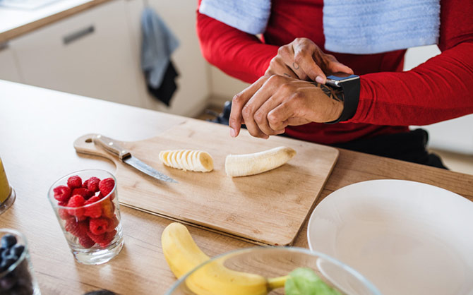 Vrouw die haar horloge controleert en een banaan eet als snack. 