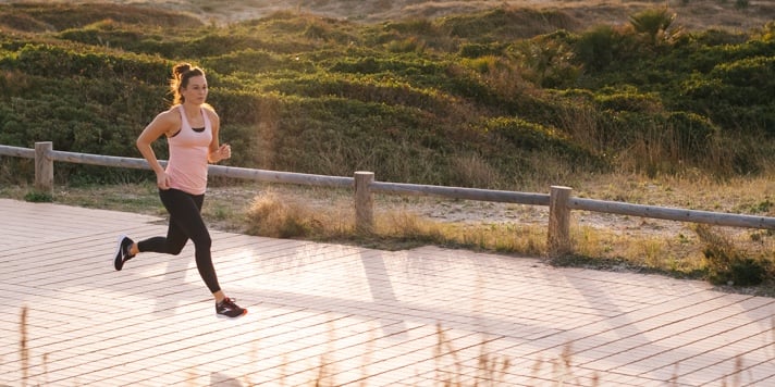 A woman runs alongside a wooden fence with greenery on the other side.