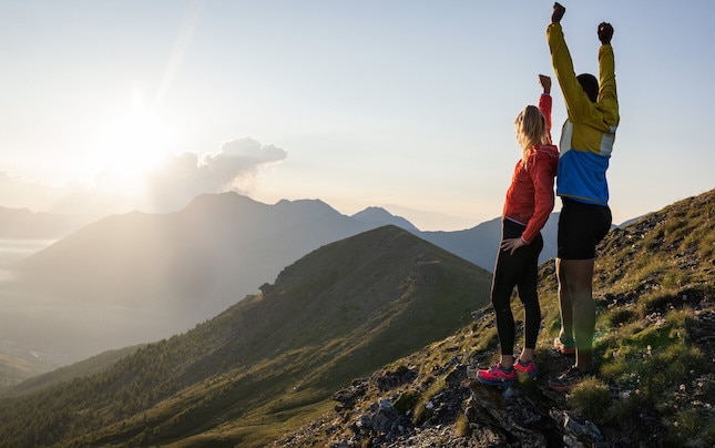 Two runners in mountains with sun coming out of the clouds