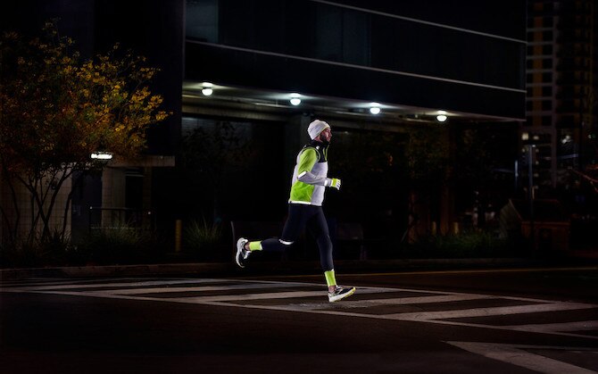 Side view of two runners running on a road at night while wearing reflective gear