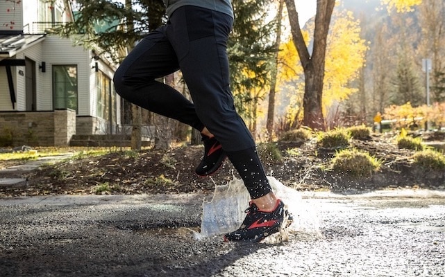 Un runner mentre compie un passo in una pozzanghera d’acqua correndo sotto la pioggia.