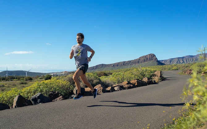 Coureur sur un chemin avec une prairie et un ciel bleu autour de lui.