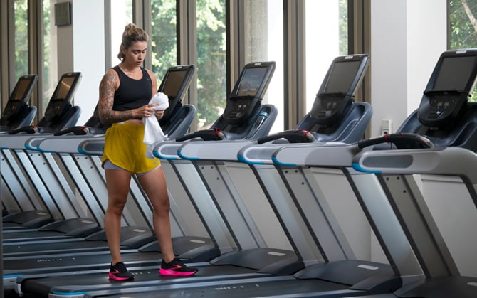 Une femme debout sur un tapis de course dans une salle de sport tenant une serviette