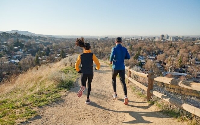 Rear view of two runners on a sandy path overlooking a city.