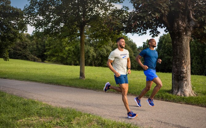 Two runners on a paved path lined with grass and trees