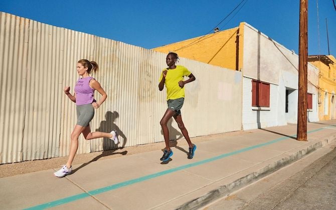Two runners on a sunny sidewalk in a city.