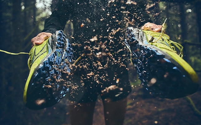 someone smacking together a pair of Cascadia 19 trail running shoes with dirt flying off the shoes