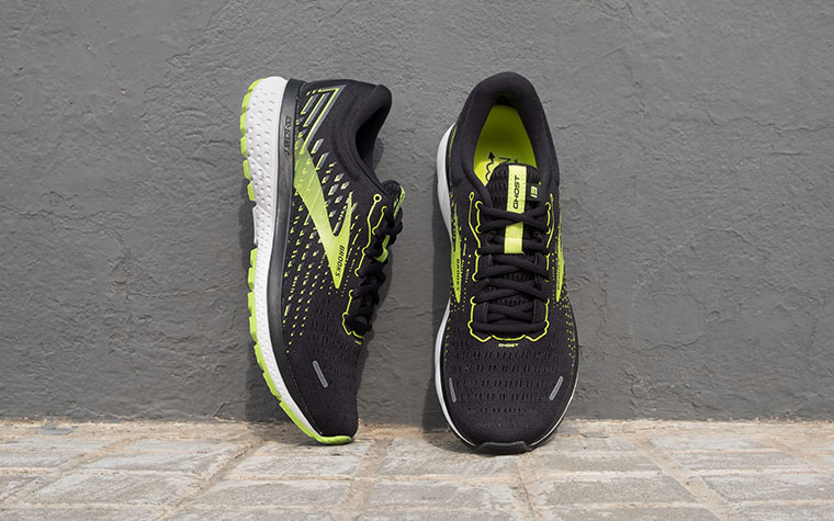 A pair of black and green Ghost shoes lean against a grey wall.