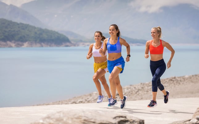 Two smiling women runners fist bump while on a trail.