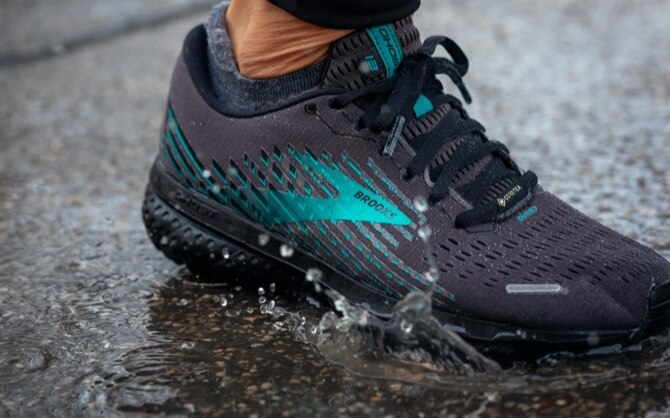 Close-up of a black and green running shoe as a runner steps on wet concrete.