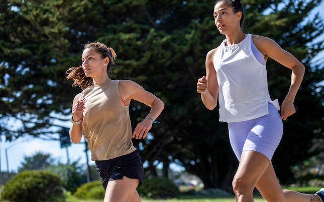 Two smiling women runners fist bump while on a trail.