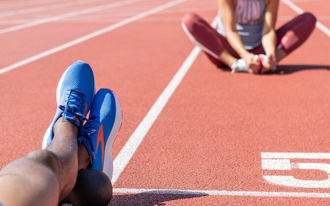 two runners sitting on a track stretching