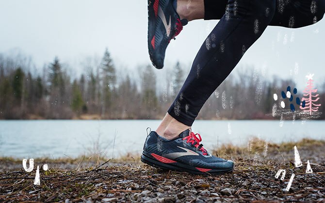 A runners legs in mid stride shown running on a wet, rocky trail next to a river. 