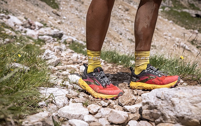 Close-up of someone wearing the Cascadia 17 trail running shoes covered in dirt at the bottom of a rocky trail
