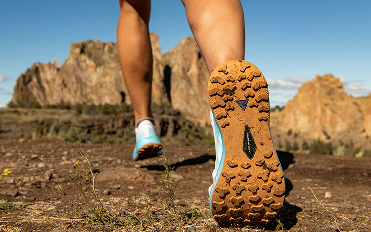 Close-up from behind a runner’s back foot, as runner strides along a trail.