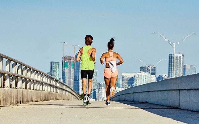 Two runners cross a bridge toward a city skyline.
